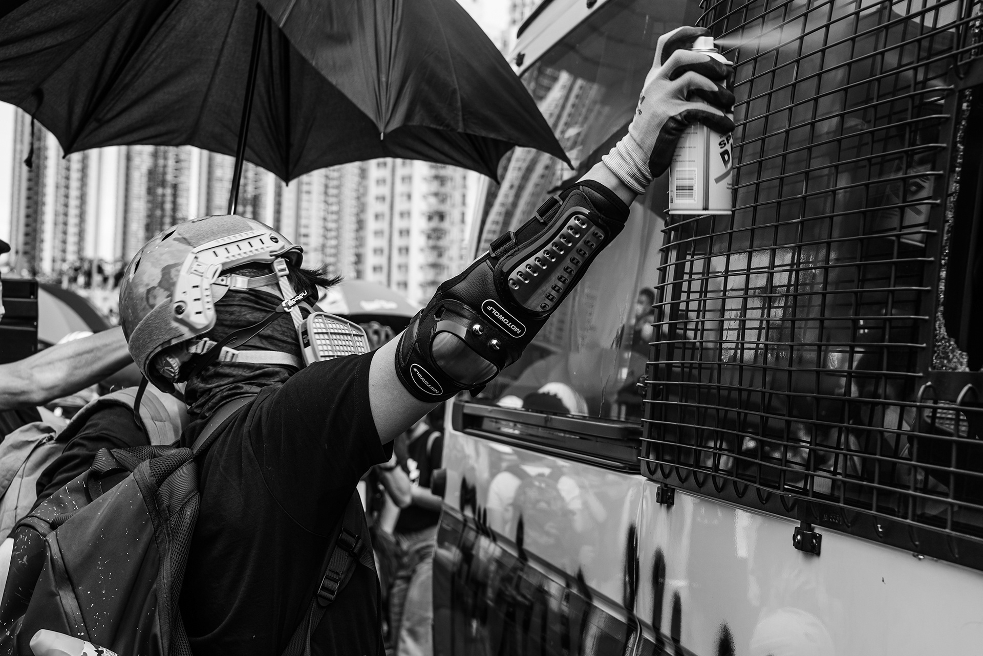 안전모와 방독면을 착용하고 경찰 차량에 스프레이를 뿌리는 시위 참가자